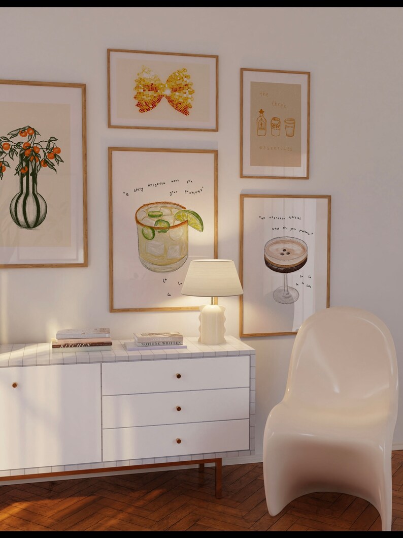May include: A white dresser with four drawers and gold handles. The dresser is decorated with white tiles. Above the dresser are eight framed illustrations, including a butterfly, a margarita, a cocktail, and a bottle of liquor. The dresser is in front of a white wall and a light wood floor.