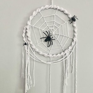 Peut inclure: Un attrape-rêves en macramé blanc avec un motif de toile d'araignée et trois araignées en plastique noir. L'attrape-rêves circulaire comporte des glands blancs suspendus. Une décoration d'Halloween.