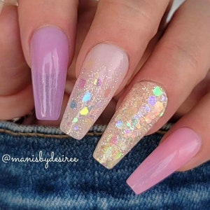 May include: Long, light pink and nude coffin-shaped nails with iridescent glitter accents. The nails are decorated with small, colorful glitter pieces.