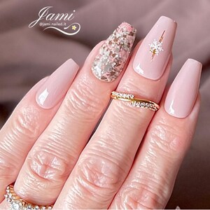 May include: Pink and nude long coffin shaped press-on nails with a gold snowflake design on one nail and a glitter design on another nail.  @jami.nailed.it