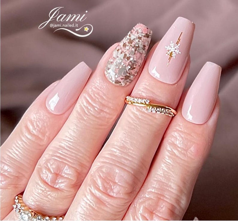 May include: Pink and nude long coffin shaped press-on nails with a gold snowflake design on one nail and a glitter design on another nail.  @jami.nailed.it