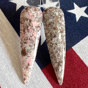 May include: Two nail polish bottles with a brown and pink glitter finish. The bottles are on a red, white, and blue background.