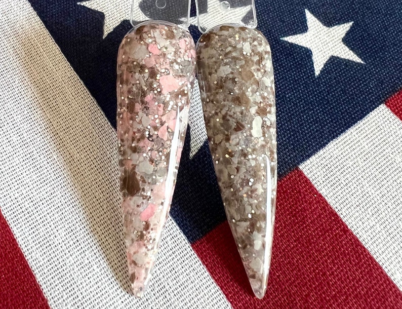 May include: Two nail polish bottles with a brown and pink glitter finish. The bottles are on a red, white, and blue background.