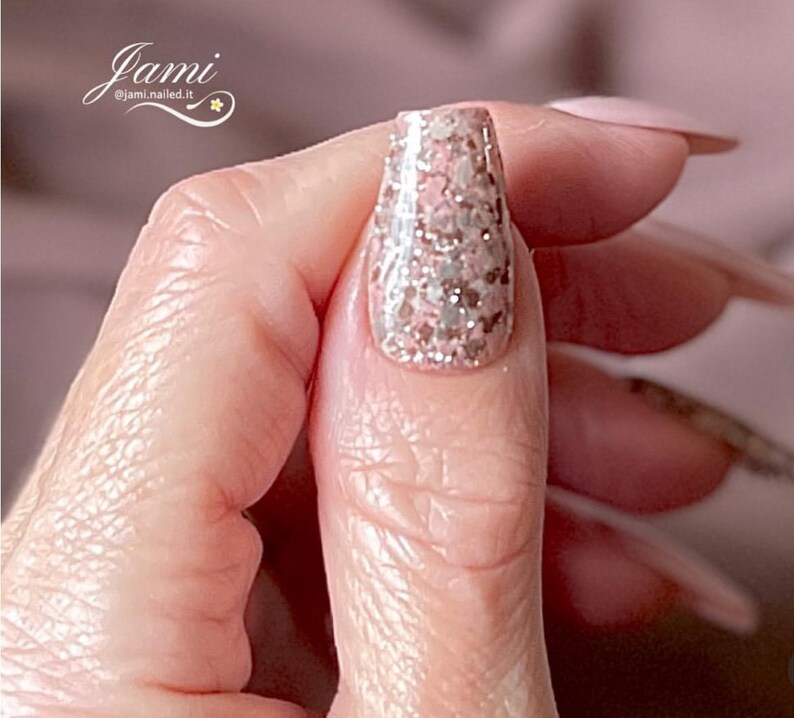 May include: Close-up of a finger with a pink and silver glitter nail polish. The nail is long and oval shaped.