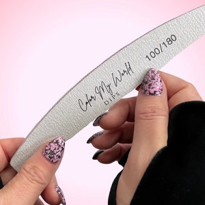 May include: A white nail file with the text "Color My World Dips" and "100/180" printed on it. The file is curved and is being held by a person.