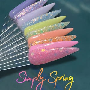 May include: A collection of ten long, pointed acrylic nail samples in a variety of pastel colors, including lavender, light blue, yellow, and pink. Each nail has a different glitter or shimmer effect. The words "Simply Spring Collection" are written in a cursive font.