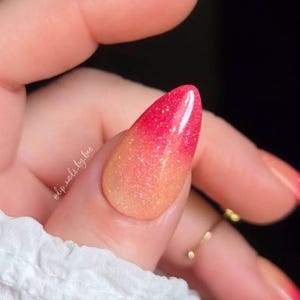 May include: Almond-shaped fingernails featuring a vibrant gradient transition from a bright, saturated pink at the tips to a soft, warm peach at the base. The entire surface is infused with fine, reflective glitter particles. Text reads @dip_nails_by_bee.
