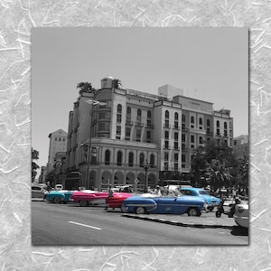 May include: A black and white photo of a vintage hotel in Havana, Cuba.  The hotel is a large, multi-story building with a classic facade.  In the foreground, there are several classic American cars parked in front of the hotel.  The cars are painted in various colors, including blue, pink, and white.