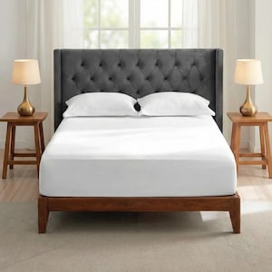 May include: A bed featuring a dark grey, button-tufted headboard and a wooden frame. The bed is made with white sheets and pillows. Two small wooden bedside tables with lamps are on either side.
