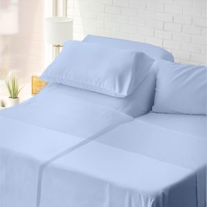 Puede incluir: Un juego de sábanas azul claro con dos fundas de almohada sobre una cama. Las sábanas están cuidadosamente dispuestas y las fundas de almohada son voluminosas. La ropa de cama está hecha de un material suave y liso. El fondo incluye una ventana y una pared de ladrillo blanco.