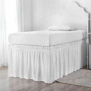 May include: A white bed skirt with a gathered, ruffled design that extends from the mattress to the floor. The bed skirt features a clean, solid white fabric that covers the base of the bed, providing a uniform look beneath the white mattress.