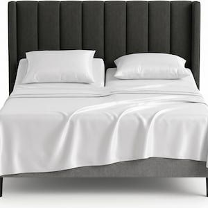 May include: A bed featuring a dark charcoal gray upholstered headboard with vertical channel tufting. The bed is dressed in smooth white sheets and two white pillows, with the mattress split into two distinct sections at the head of the frame.