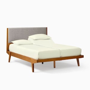 May include: A split king bed with a light wood frame and a gray upholstered headboard. The bed has two separate mattresses covered with cream-colored sheets and two matching pillows. The bed frame has angled legs.