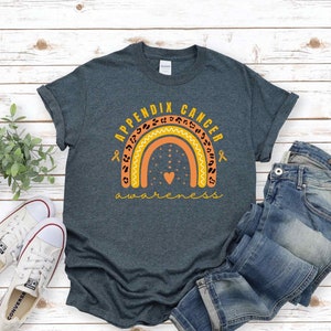 Könnte beinhalten: Ein dunkelblaues T-Shirt mit dem Text "Appendix Cancer Awareness" und einem Regenbogen mit einem Herz in der Mitte. Der Regenbogen ist mit orangefarbenen und gelben Zickzacklinien und schwarzen Leopardenflecken verziert.