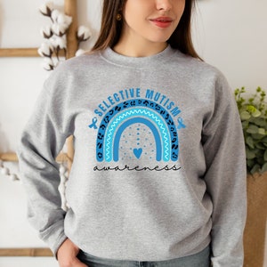 May include: A gray sweatshirt with a blue and turquoise rainbow design. The rainbow has a leopard print pattern and the words "Selective Mutism awareness" are printed above and below the rainbow in blue and black.