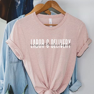 Op de afbeelding: Perzikkleurig T-shirt met de tekst "LABOR & DELIVERY surgical technologist" in zwarte letters.
