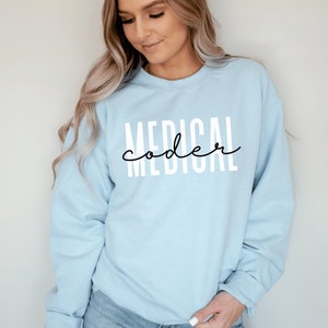 Puede incluir: Una sudadera azul claro con el texto "MEDICAL coder" impreso en blanco en la parte delantera.