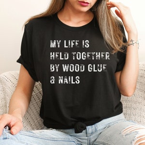 May include: A black t-shirt with the text "My life is held together by wood glue & nails" in white lettering.