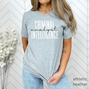 May include: A gray t-shirt with the text "CRIMINAL analyst INTELLIGENCE" printed in black.