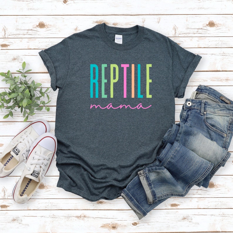 May include: A dark heather grey t-shirt with the text "REPTILE mama" in rainbow colors. The text is in a vertical stacked format with each letter in a different color.