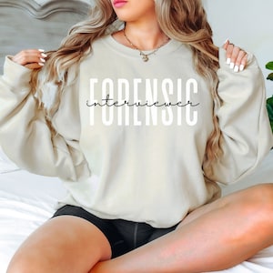 May include: A beige sweatshirt with the text "FORENSIC interviewer" printed in white on the front.