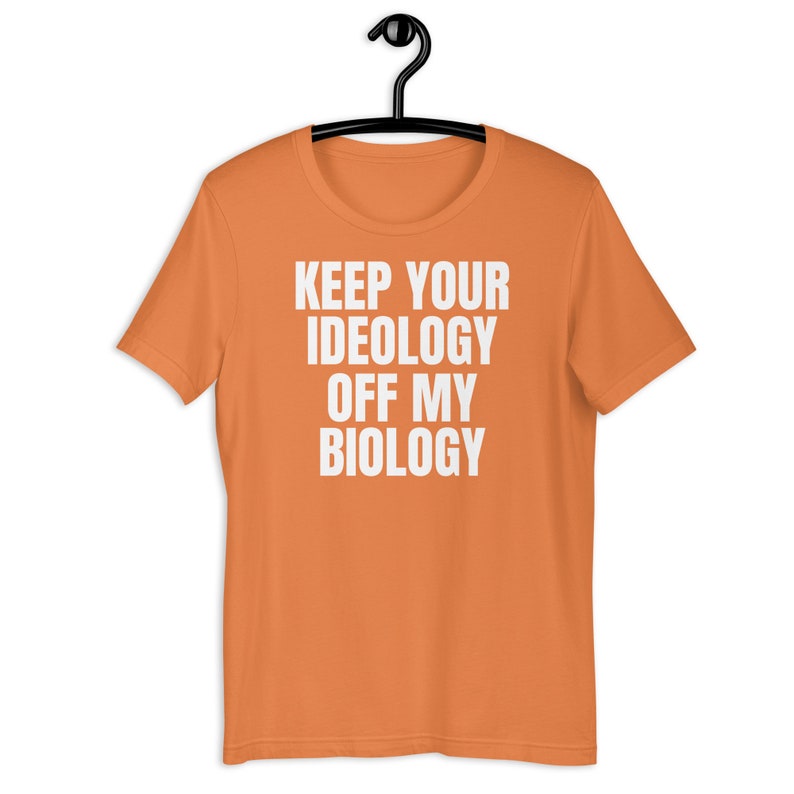 May include: Orange short-sleeved t-shirt with the text "KEEP YOUR IDEOLOGY OFF MY BIOLOGY" printed in white.