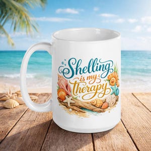 May include: White ceramic mug with the text "Shelling is my Therapy" in teal and gold script, decorated with seashells, starfish, and a piece of driftwood. The mug is set on a wooden surface with a beach scene in the background.