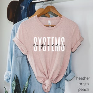 May include: A heather prism peach colored t-shirt with the text "SYSTEMS engineer" printed in black on the front.