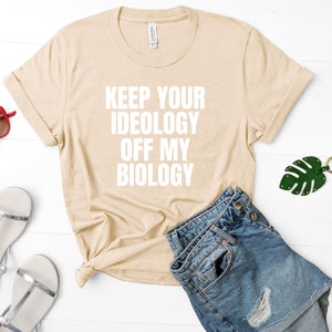 May include: A beige t-shirt with the text "KEEP YOUR IDEOLOGY OFF MY BIOLOGY" printed in white.