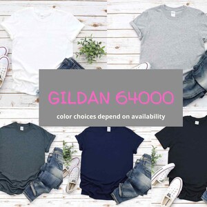 May include: Five blank Gildan 64000 t-shirts in different colors: white, heather gray, dark heather, navy blue, and black. Each shirt is folded and placed on a wooden surface with a pair of jeans.