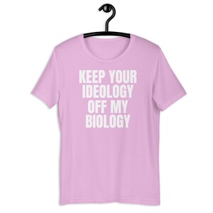 May include: A pink t-shirt with the text "KEEP YOUR IDEOLOGY OFF MY BIOLOGY" printed in white.