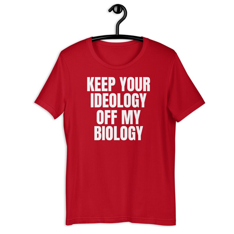 May include: Red t-shirt with white text that reads "Keep your ideology off my biology."