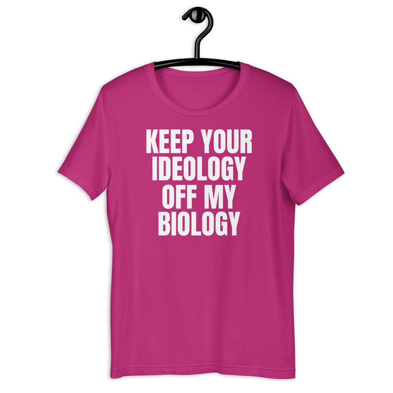 May include: Pink t-shirt with the text "KEEP YOUR IDEOLOGY OFF MY BIOLOGY" in white.