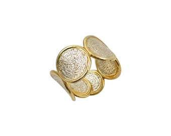 Puede incluir: Un brazalete dorado con múltiples elementos circulares en forma de monedas. Cada disco tiene una superficie texturizada y detallada con un diseño en relieve. El brazalete se presenta sobre un fondo blanco, resaltando su brillo metálico y sus intrincados detalles.