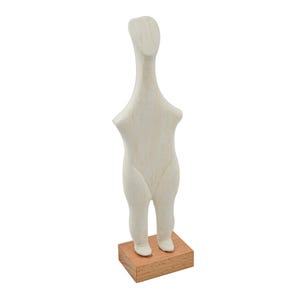 Op de afbeelding: Een crèmekleurige, abstracte sculptuur van een menselijke figuur. De figuur heeft een lange nek, een afgeronde torso en korte benen. Hij staat op een kleine, rechthoekige houten basis. De sculptuur is glad en minimalistisch van ontwerp.