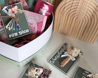 May include: A heart-shaped gift box filled with pink items, including a can of Rosé and a box of Yoguette. Several green cards with floral arrangements and German text are displayed, including "FÜR DICH" and "alles LIEBE."