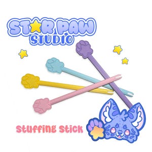 May include: Four stuffing sticks in yellow, light blue, purple, and pink, each featuring a paw-shaped handle with a star center. The text STAR PAW STUDIO and STUFFING STICK appears alongside a cartoon illustration of a blue creature with large eyes.