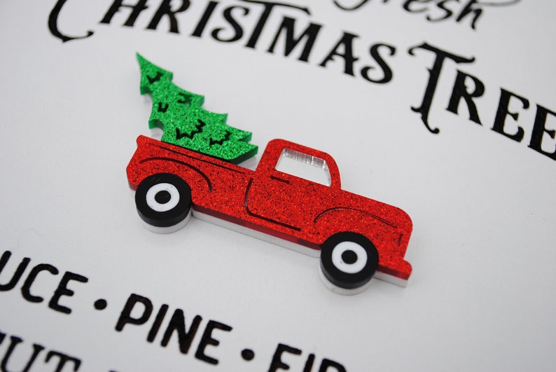 Puede incluir: Una camioneta roja con un &aacute;rbol de Navidad verde en la caja. La camioneta est&aacute; hecha de purpurina y tiene ruedas blancas. El texto "Fresh Christmas Tree" es visible en el fondo.