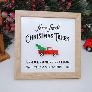 Puede incluir: Un cartel enmarcado con el texto "farm fresh CHRISTMAS TREES" y un cami&oacute;n de juguete rojo que lleva un &aacute;rbol de Navidad verde. El cartel tambi&eacute;n incluye el texto "SPRUCE - PINE - FIR - CEDAR - CUT AND CARRY - "