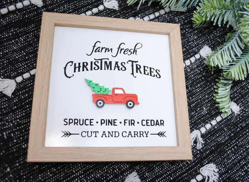 Puede incluir: Un cartel enmarcado con el texto "farm fresh CHRISTMAS TREES" y un cami&oacute;n rojo con un &aacute;rbol de Navidad en la caja. El cartel tambi&eacute;n dice "SPRUCE - PINE - FIR - CEDAR" y "CUT AND CARRY".