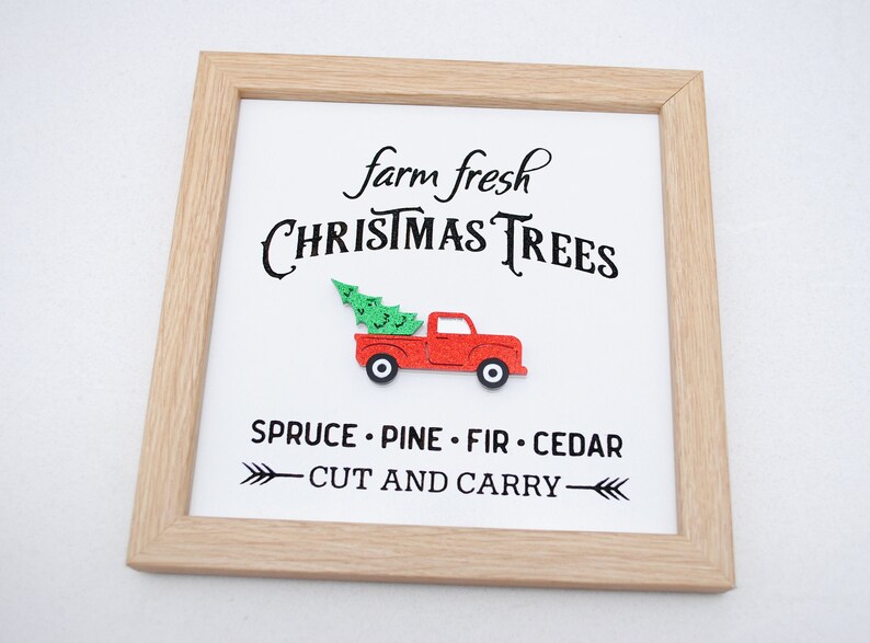 Puede incluir: Un cartel enmarcado con el texto "farm fresh CHRISTMAS TREES" y un cami&oacute;n rojo con un &aacute;rbol de Navidad en la caja. El cartel tambi&eacute;n dice "SPRUCE - PINE - FIR - CEDAR" y "CUT AND CARRY" con flechas.