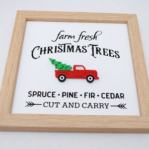 Puede incluir: Un cartel enmarcado con el texto "farm fresh CHRISTMAS TREES" y un cami&oacute;n rojo con un &aacute;rbol de Navidad en la parte trasera. El cartel tambi&eacute;n dice "SPRUCE - PINE - FIR - CEDAR" y "CUT AND CARRY" con flechas.