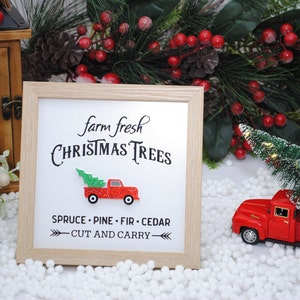 Puede incluir: Un cartel enmarcado con el texto "farm fresh CHRISTMAS TREES" y un cami&oacute;n rojo con un &aacute;rbol de Navidad en la caja. El cartel tambi&eacute;n dice "SPRUCE - PINE - FIR - CEDAR" y "CUT AND CARRY".