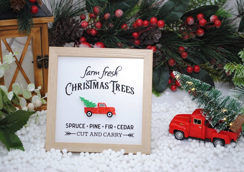 Puede incluir: Un cartel enmarcado con el texto "farm fresh CHRISTMAS TREES" y un cami&oacute;n rojo con un &aacute;rbol de Navidad en la caja. El cartel tambi&eacute;n dice "SPRUCE - PINE - FIR - CEDAR" y "CUT AND CARRY".