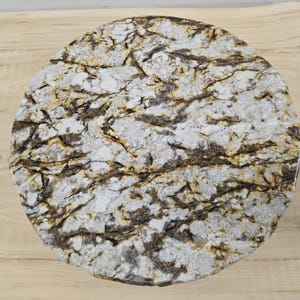 May include: A circular table top with a granite effect. The surface has a mottled pattern in shades of white, brown, and gold, resembling natural stone. The table top is round and likely made from a robust material, with a diameter of approximately 76 cm.