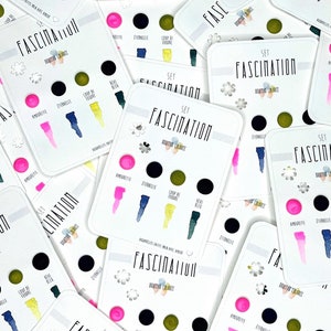 May include: Close-up of several cards with the word "Fascination" printed on them. Each card features a set of five watercolor paint swatches with names like "Amourette", "Eternelle", and "Coup de Foudre".