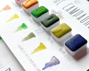 May include: A watercolor paint set titled SET NID DE CAMPAGNE featuring six rectangular pans in red, orange, bright green, dark green, olive, and navy blue. Each color is labeled with French text and includes a corresponding hand-painted swatch.