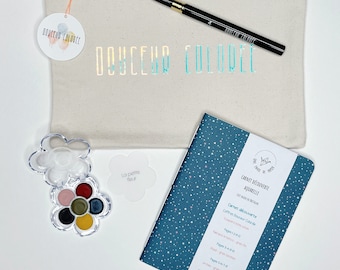 May include: A watercolour set with a blue and white star patterned notebook, a small flower-shaped watercolour palette, and a black paintbrush. The notebook says "Carnet Découverte Aquarelle" and "Coffret Douceur Colore".