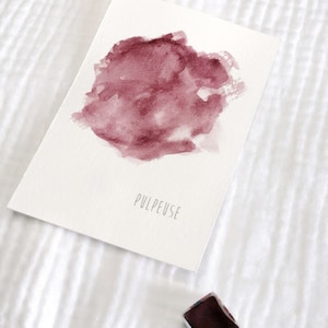 Puede incluir: Una pintura de acuarela de un lavado de acuarela rosa y morado sobre papel blanco. La palabra "PULPEUSE" está escrita en tinta negra debajo del lavado.