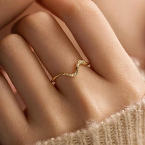 Peut inclure: Une bague dorée avec un motif ondulé, sertie de petits pierres précieuses transparentes. La bague est portée au doigt, mettant en valeur son style délicat et élégant. Le design de la bague est un bijou subtil mais accrocheur.